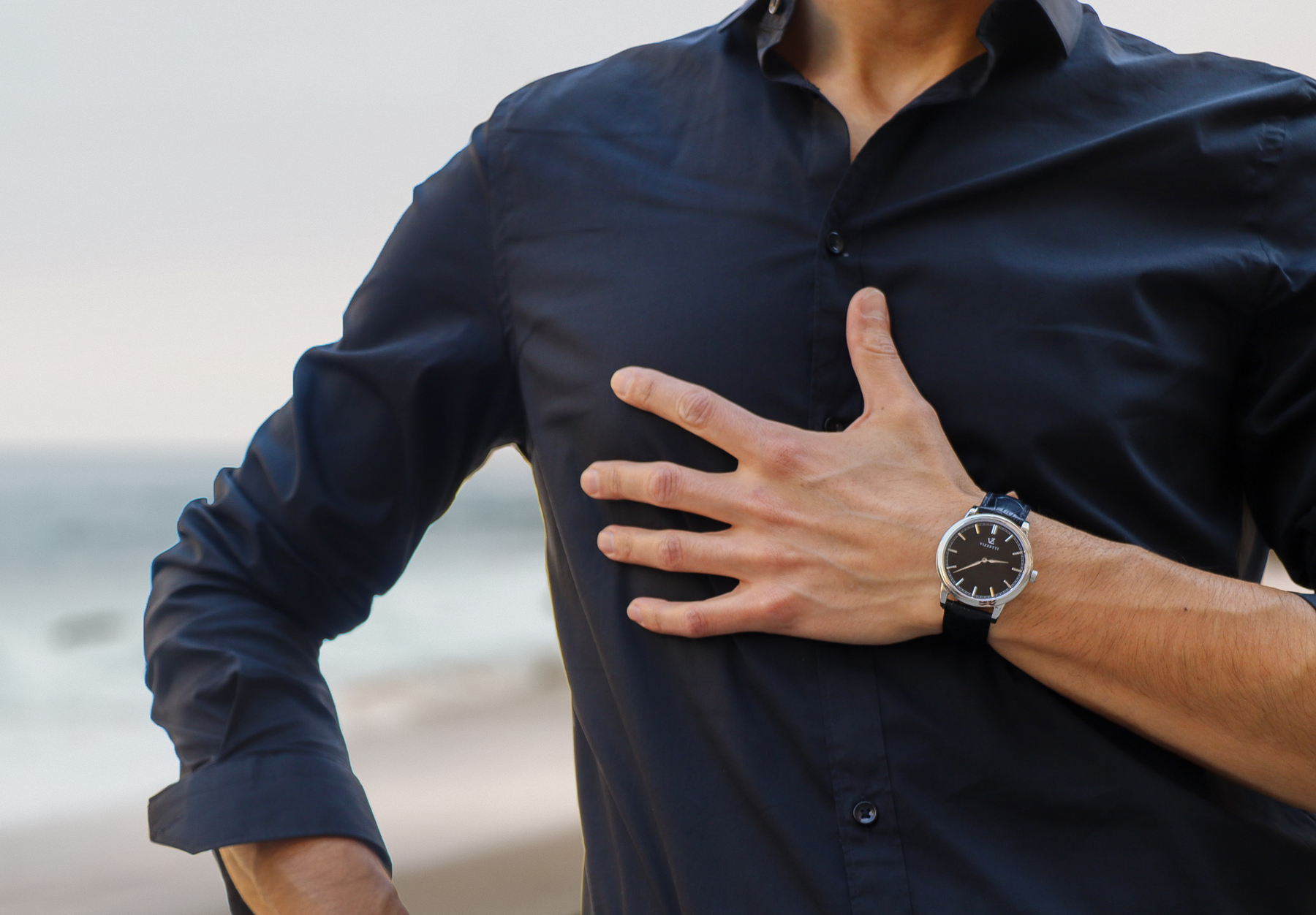 A male model poses on the beach, displaying his Vizzetti watch on his wrist.